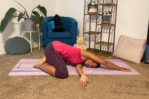 Coach Breanna, a black female in a pink shirt and maroon leggings in a thread the needle child's pose variation.